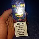 A hand holding a colorful vape box with a warning label stating, "This product contains nicotine. Nicotine is an addictive chemical."