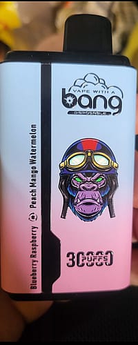 A close-up of a disposable vape device with a design featuring a purple gorilla wearing goggles. The text "Vape with a Bang" is visible at the top, and flavors like "Blueberry Raspberry" and "Peach Mango Watermelon" are listed. The device also indicates "3000 Puffs" at the bottom.
