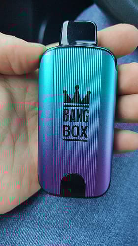 A hand holding a small metallic device labeled "BANG BOX" with a crown icon on the front.