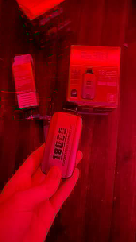 A hand holding a vape device labeled "1800 puffs" in a red-lit environment, with packaging and other vape items visible in the background.