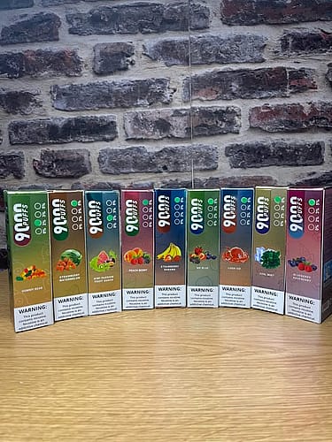 A row of vape boxes with different fruit and mint flavors displayed against a brick wall.