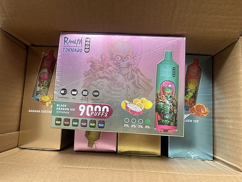 A cardboard box containing various flavors of RandM Tornado disposable vape devices, with the box for "Black Dragon Ice" flavor prominently displayed, showing 9,000 puffs and nicotine strength options.