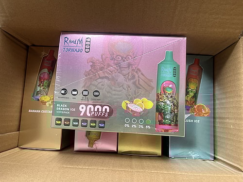 A cardboard box containing various flavors of RandM Tornado disposable vape devices, with the box for "Black Dragon Ice" flavor prominently displayed, showing 9,000 puffs and nicotine strength options.