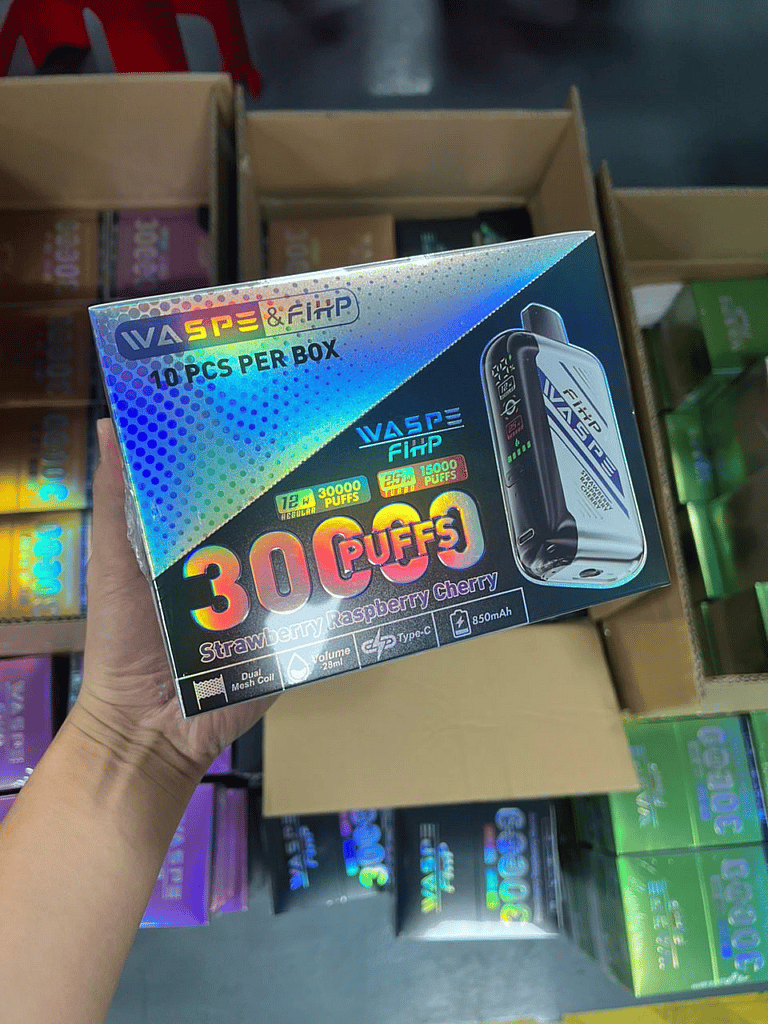 Waspe FIHP 30K Puffs Disposable Vape photos - SleekVape A hand holding a box of WASPE & FiHP vape devices labeled "30000 puffs, strawberry raspberry cherry flavor, 850mAh, Type-C, 28ml, dual mesh coil," with multiple boxes in the background.