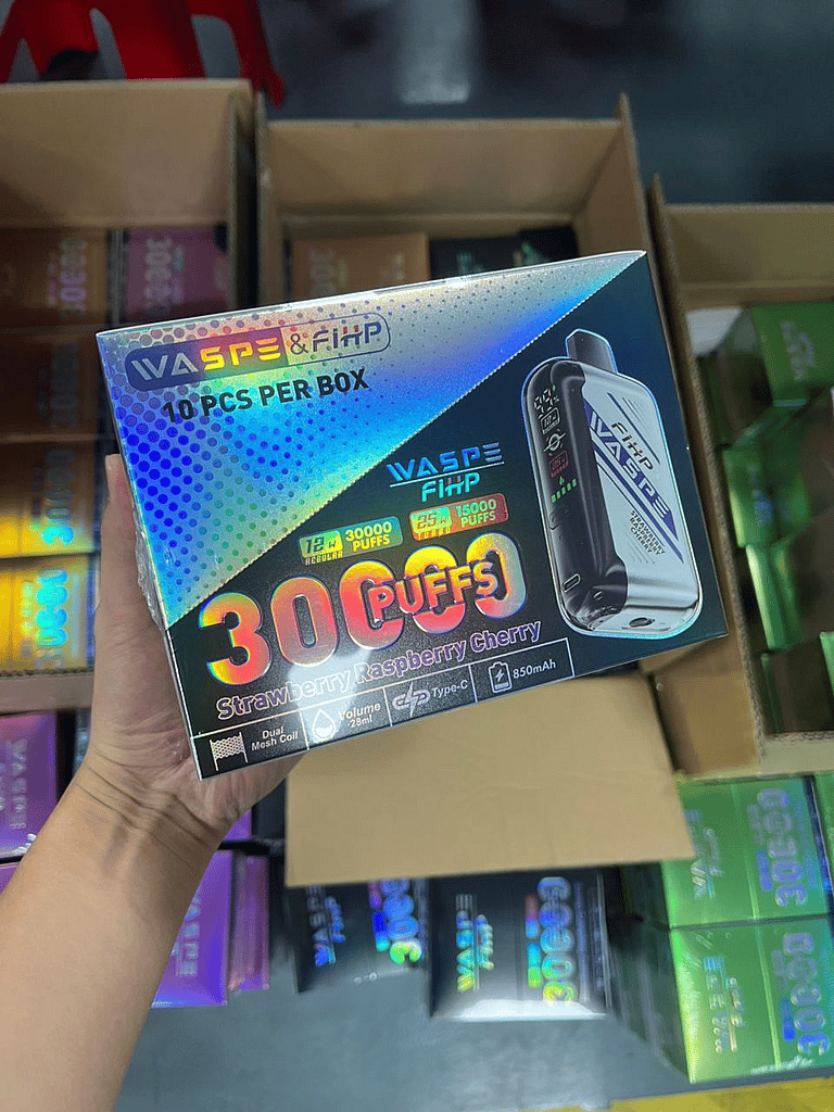 Waspe FIHP 30K Puffs Disposable Vape photos - SleekVape A hand holding a box of WASPE & FiHP vape devices labeled "30000 puffs, strawberry raspberry cherry flavor, 850mAh, Type-C, 28ml, dual mesh coil," with multiple boxes in the background.