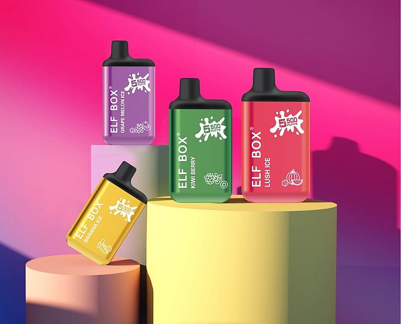 Four colorful ELF BOX vape devices on a multi-level pastel podium, with flavors labeled as Grape Melon Ice, Kiwi Berry, Lush Ice, and Banana Ice, against a vibrant gradient background.
