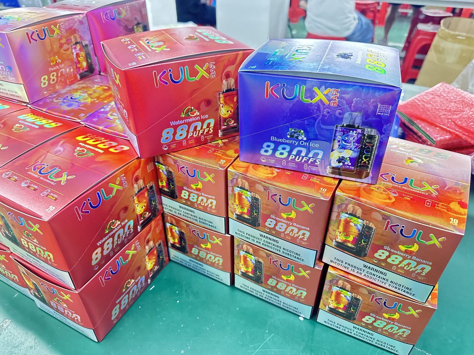 Stacks of colorful KULX Bar disposable vape boxes in various flavors, including Watermelon Ice, Blueberry On Ice, and Strawberry Banana, each labeled with "88,000 puffs" and nicotine warnings.