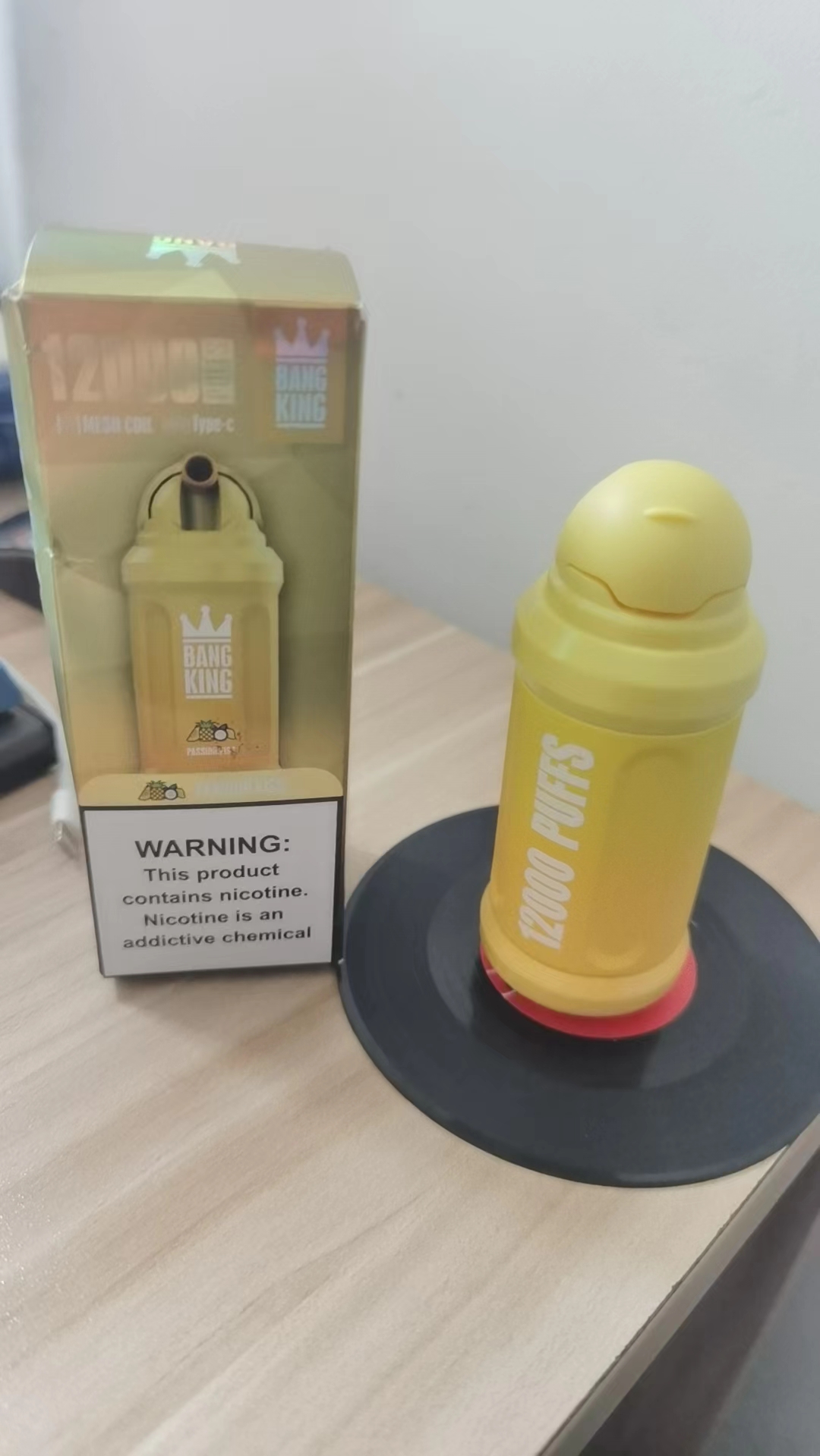 Yellow vaping device labeled "12000 PUFFS" next to its packaging with a nicotine warning.