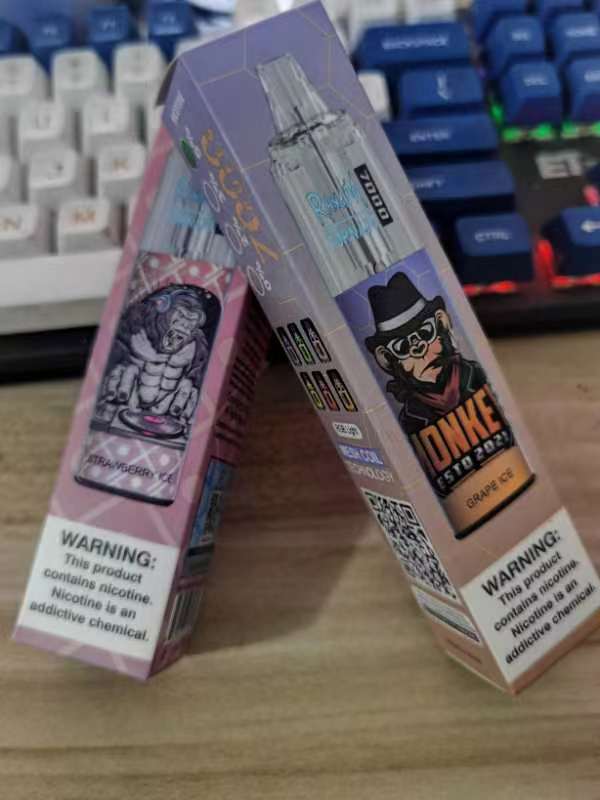 Two boxed vape products with cartoon-style packaging, placed leaning against each other on a desk.