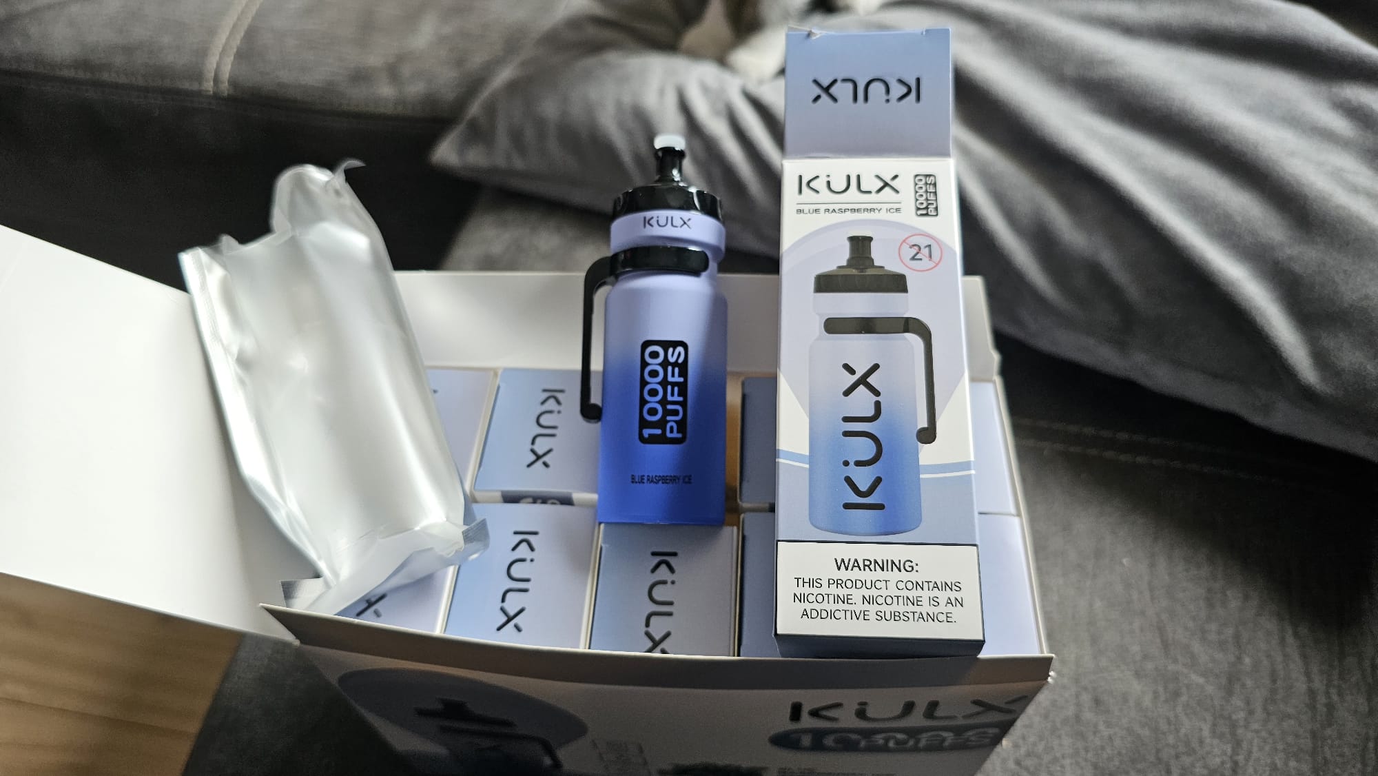 A box containing multiple KULX Blue Raspberry Ice disposable vape devices, each labeled with "10000 PUFFS" and a nicotine warning.