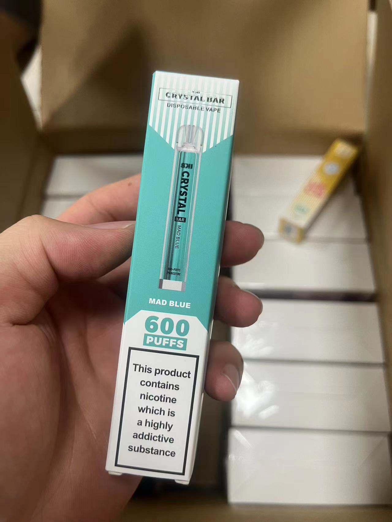 A hand holding a "Crystal Bar" disposable vape box labeled "Mad Blue," with "600 PUFFS" and a nicotine warning.