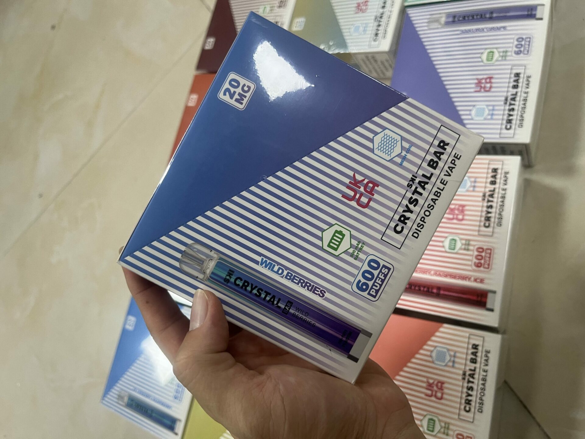 A person holding a box of Crystal Bar disposable vape with "Wild Berries" flavor, 20mg nicotine strength, and 600 puffs written on the packaging.