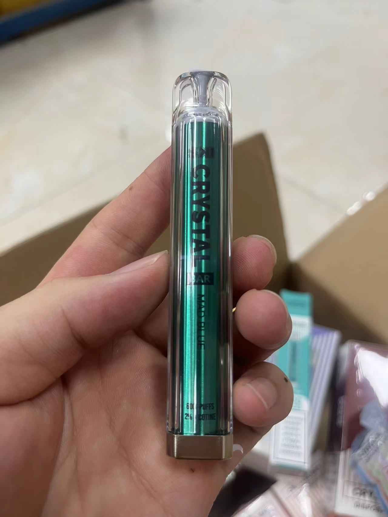 A person holding a green, transparent disposable vape labeled "CRYSTAL" with "6000 PUFFS" and "2% NICOTINE" written on it.