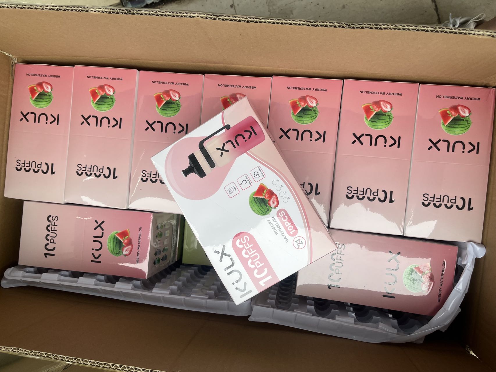 A box containing multiple pink packages of KULX 10,000 Puffs disposable vapes with watermelon flavor.