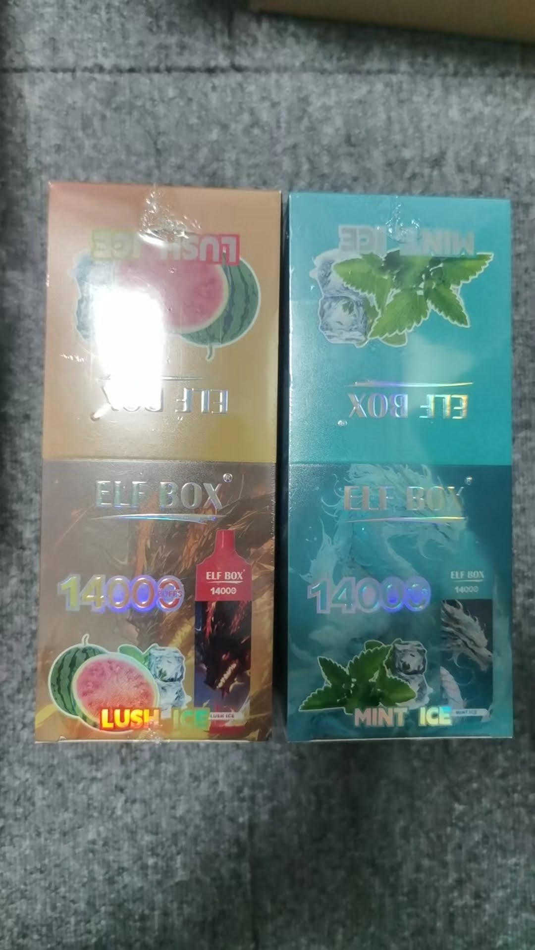 Two boxed products labeled "ELF BOX 14000," one in "Lush Ice" flavor with watermelon imagery, the other in "Mint Ice" flavor with mint leaf imagery.