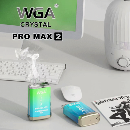 A desktop scene featuring a WGA Crystal Pro Max 2 vape device emitting vapor, with another similar device lying beside it, a wireless mouse, a keyboard, a humidifier, and a magazine on the desk.