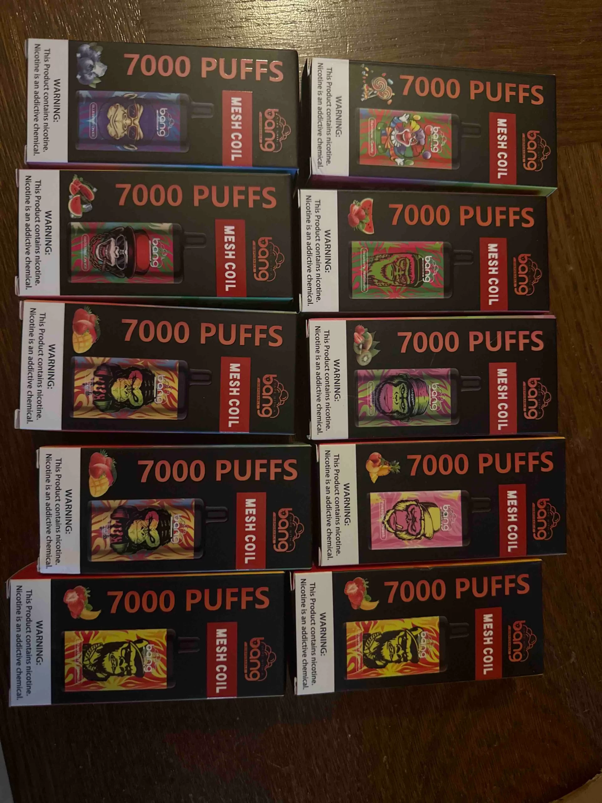 Boxes of "BANG" brand disposable vapes with various designs, labeled "7000 PUFFS" and "MESH COIL," displayed in a 3x4 arrangement.