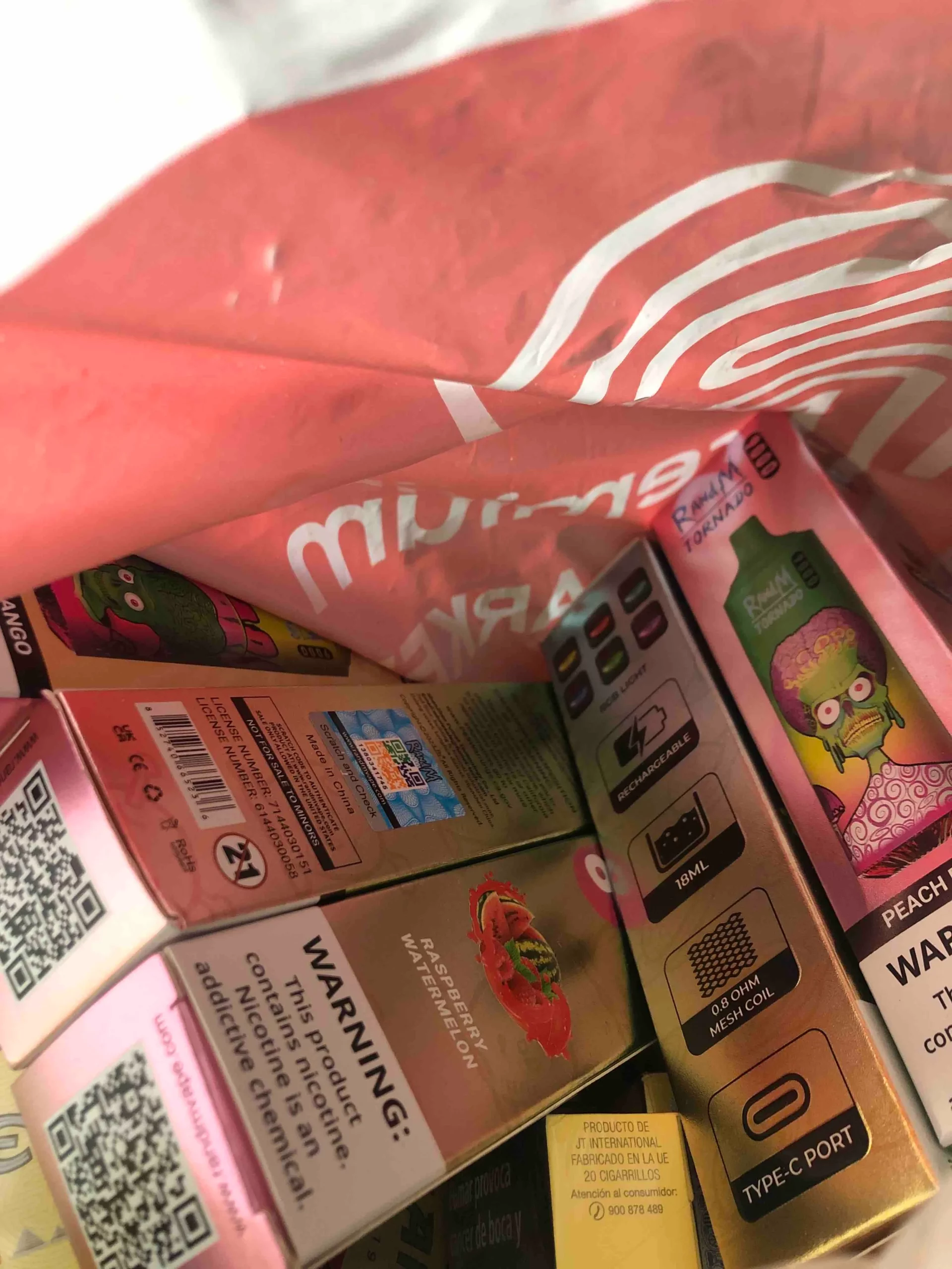 Boxes of flavored disposable vapes, including "Raspberry Watermelon" and "Peach Ice," inside a pink bag.