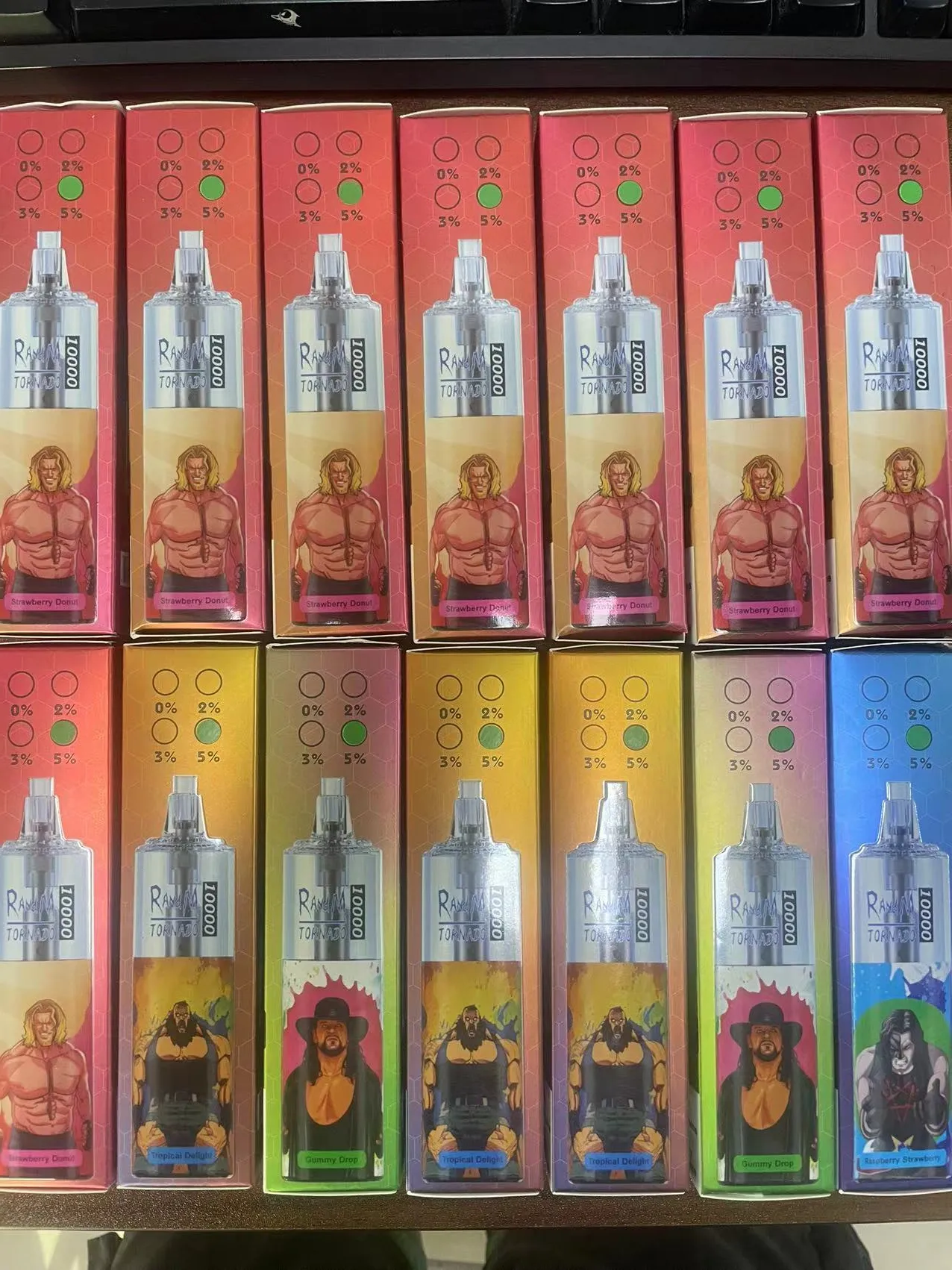 A collection of twelve vape boxes with various designs and flavors, featuring illustrations of muscular characters on the packaging, including themes of "Strawberry Donut," "Tropical Delight," "Gummy Drop," and "Blueberry Strawberry."