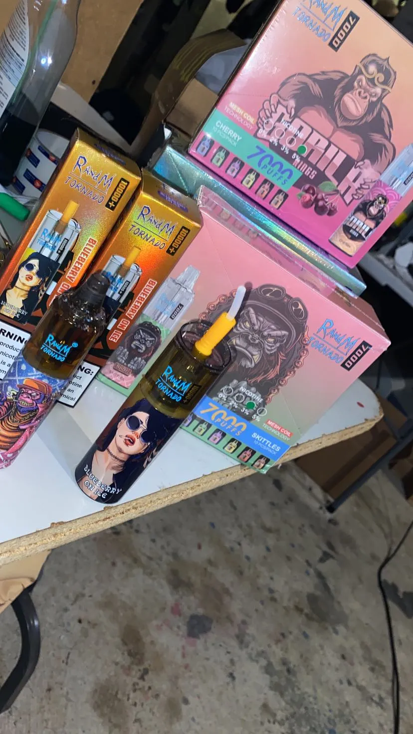 Boxes and bottles of flavored e-liquids with colorful packaging displayed on a table, featuring brand names, cartoonish characters, and nicotine strength information.