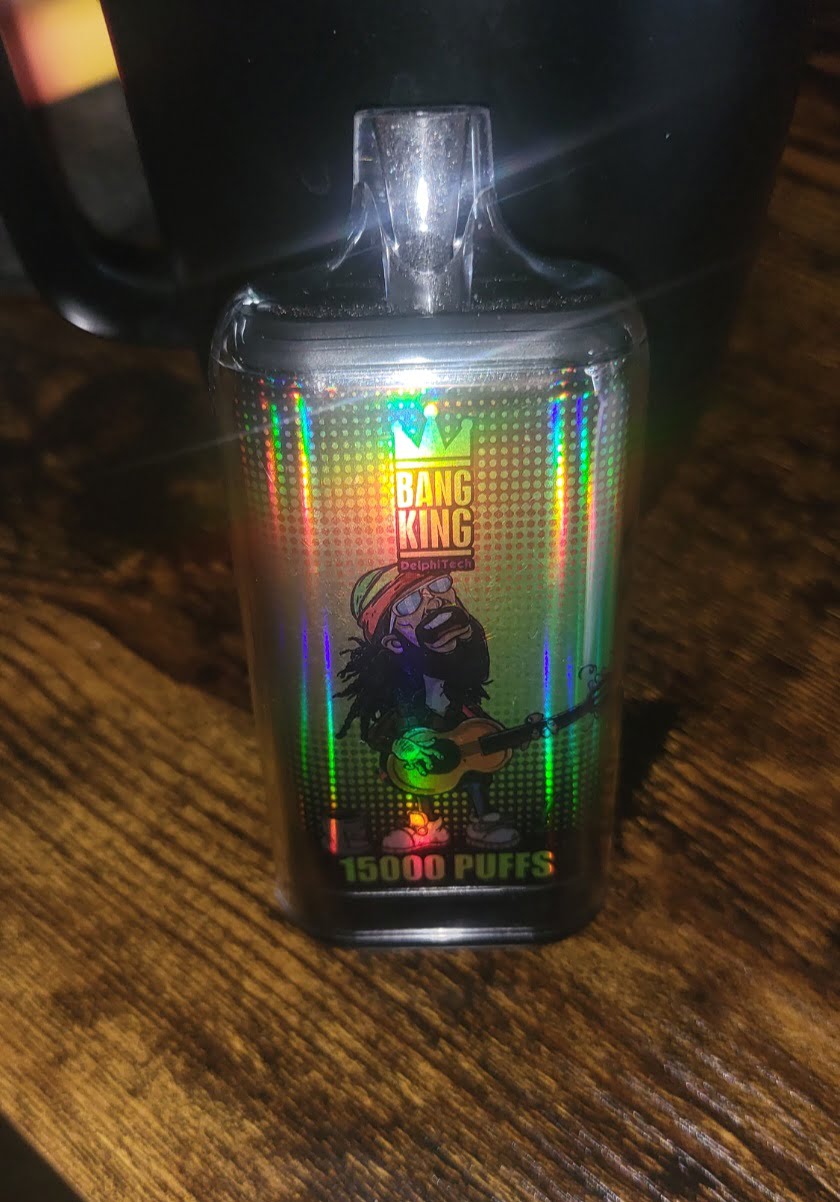 A holographic vape device labeled "Bang King DelphiTech 15000 PUFFS" featuring an illustration of a man playing a guitar.