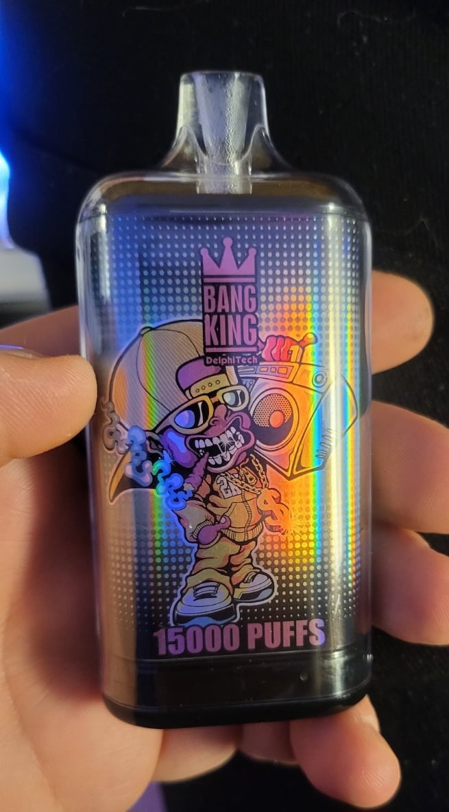 A close-up of a hand holding a vape device labeled "BANG KING DelphiTech" with colorful artwork of a cartoon character and the text "15000 PUFFS" at the bottom.