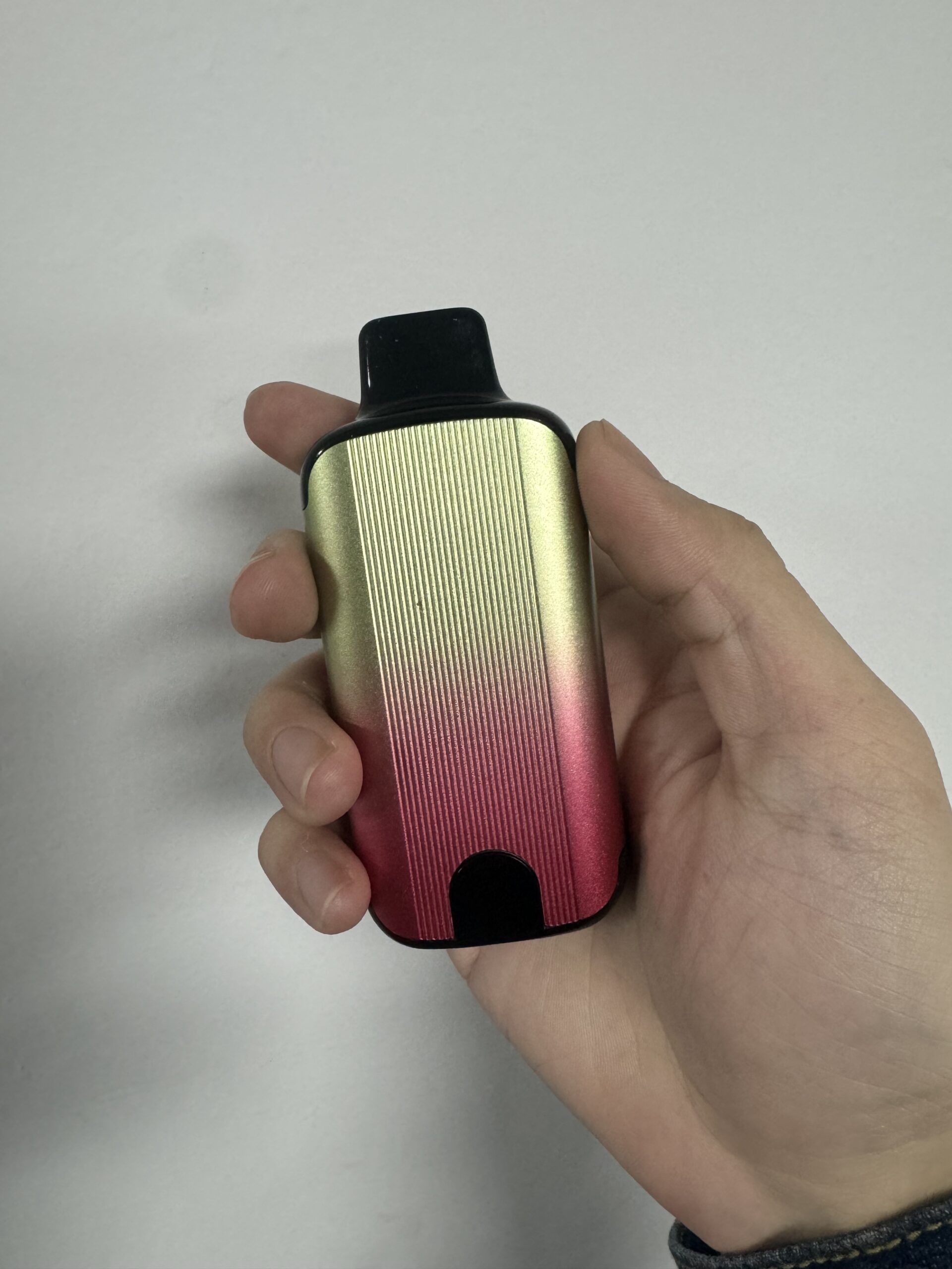 A hand holding a small, gradient-colored vape device with gold and red tones, featuring a black mouthpiece.