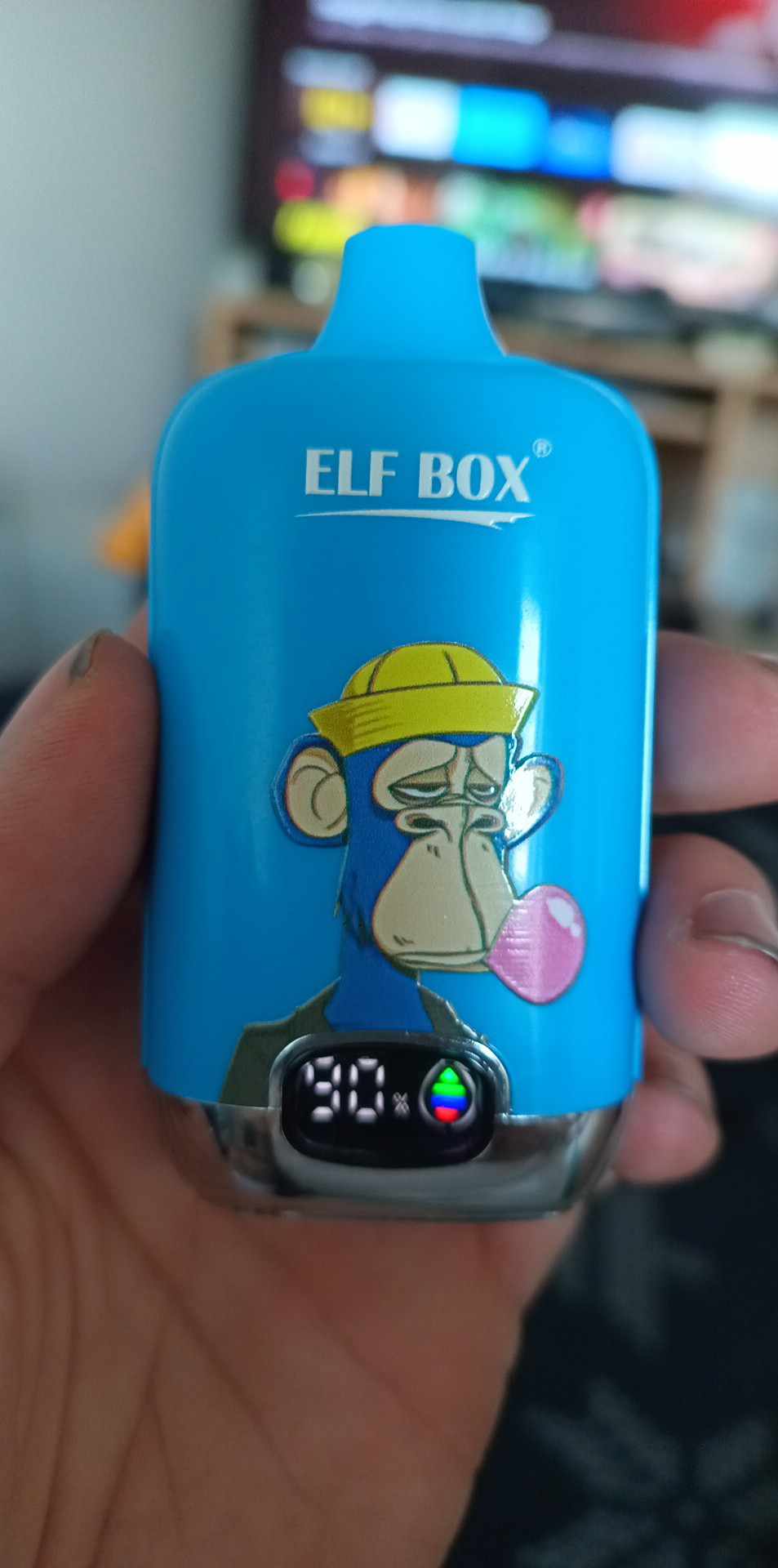 Blue "Elf Box" vaping device with a cartoon image of a monkey wearing a yellow hat and chewing bubblegum, showing a battery indicator on the screen.