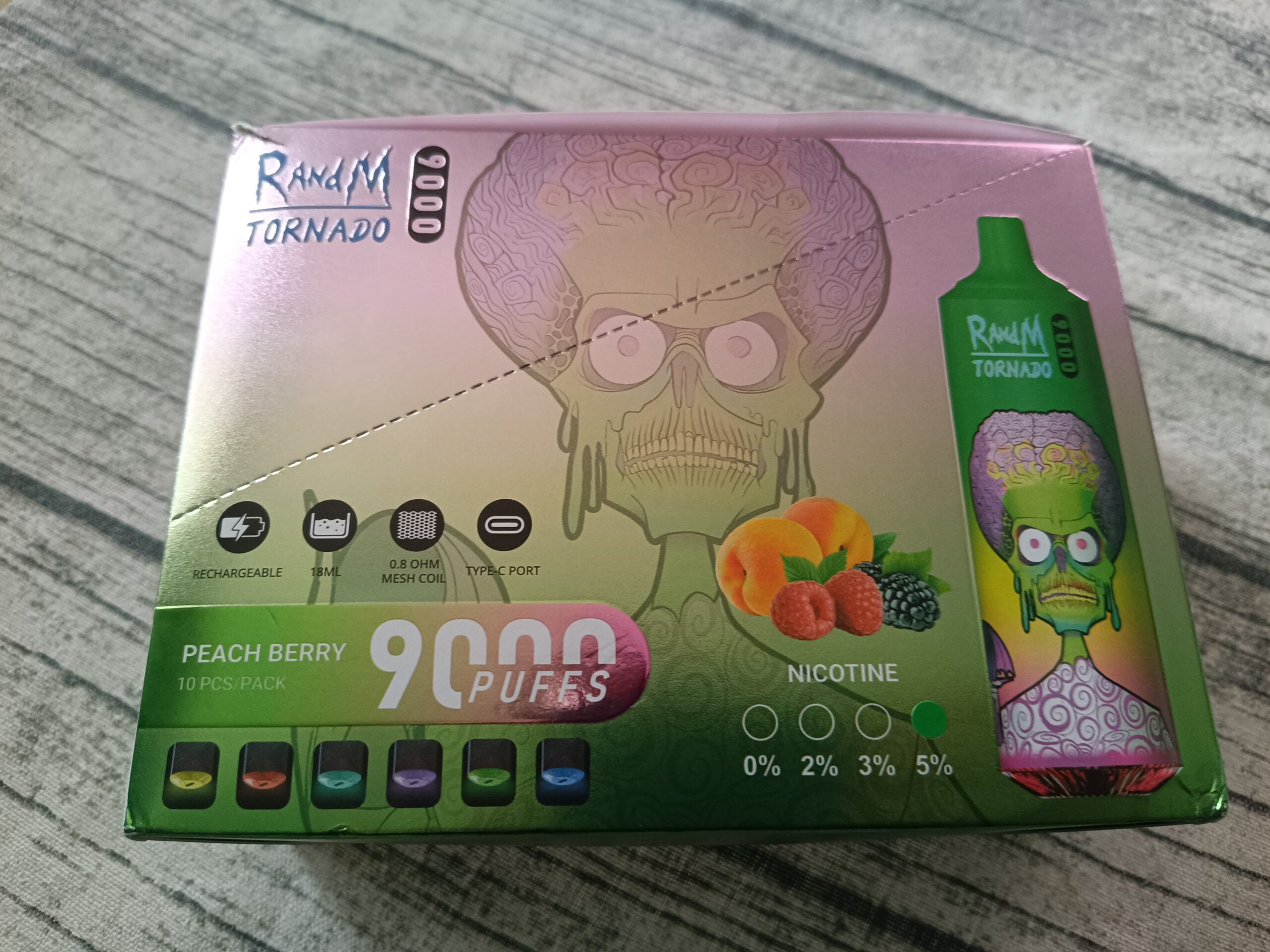 Packaging of a RandM Tornado vape device in Peach Berry flavor, featuring a green zombie-like character, with details on 9000 puffs, 18ml capacity, 0.8 ohm mesh coil, Type-C port, and 5% nicotine strength.