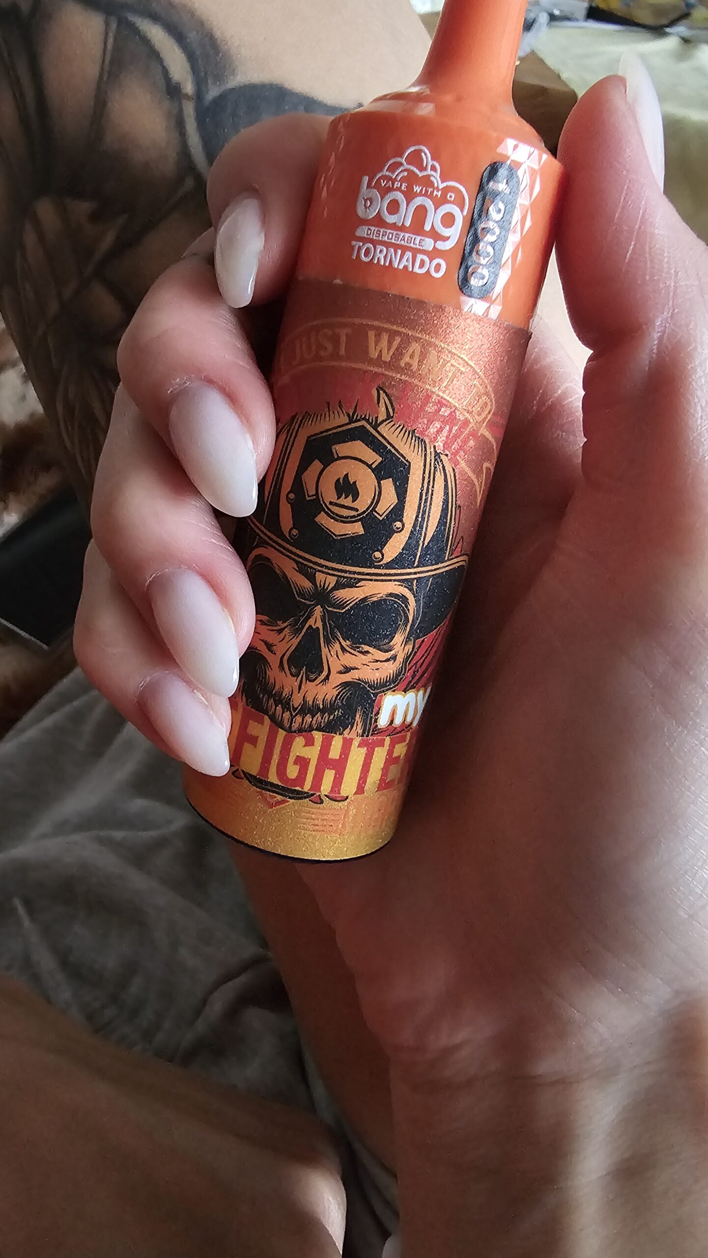 A hand holding an orange Bang Tornado disposable vape with a skull wearing a firefighter helmet on the design.