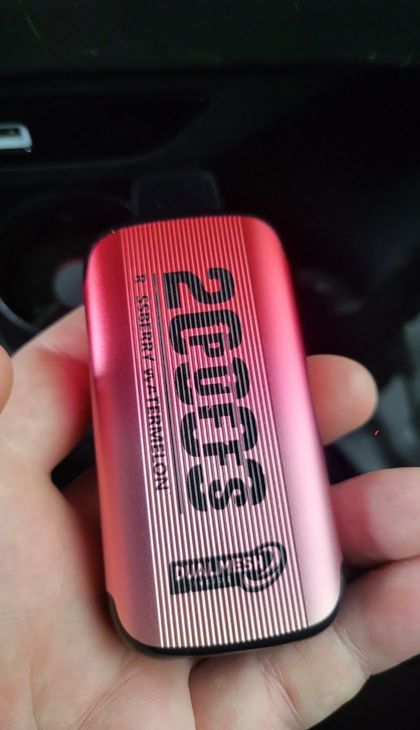 A close-up of a red and pink metallic device labeled "2000 PUFFS" with "R.S.SBERRY W.W.MERMELON" and "DUAL MESH technology" printed on it.