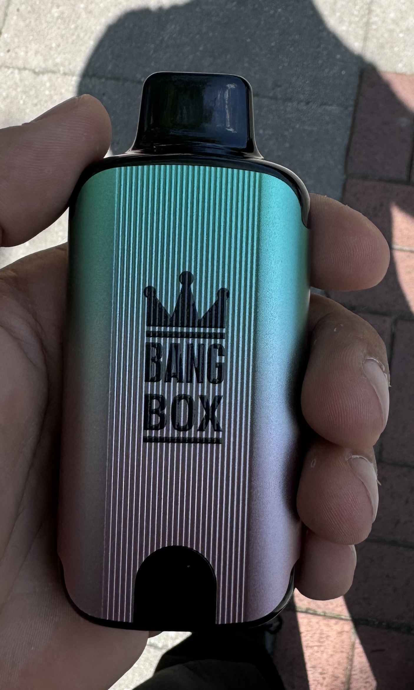 A person holding a small, metallic, gradient-colored vape device labeled "BANG BOX" with a crown logo.