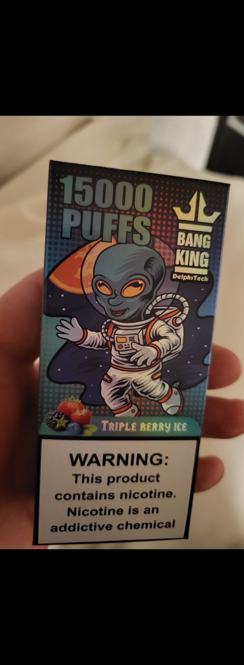 A box of "Bang King" disposable vape, featuring an alien character in a spacesuit, labeled with "15000 PUFFS" and "Triple Berry Ice" flavor, and a nicotine warning at the bottom.